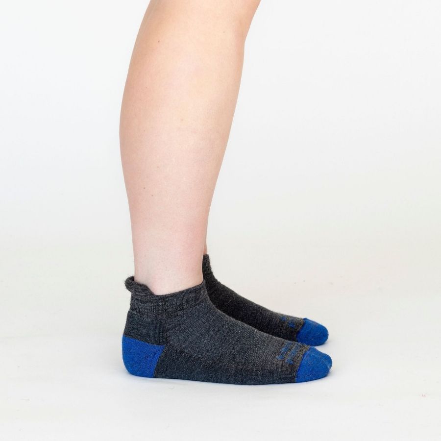 A side view of a person&#39;s lower legs with a white background wearing a pair of Alpacas of Montana soft comfortable breathable athletic outerwear activewear moisture wicking antimicrobial gray and royal blue swift wicking running sock for running, sports, hiking, exercise.