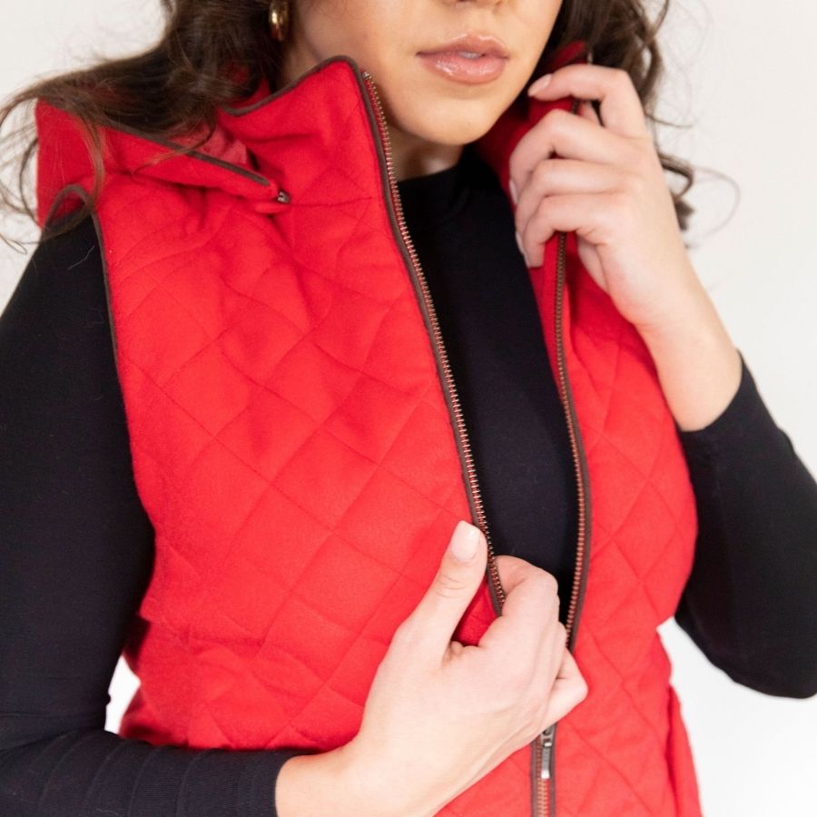 A close up on a woman with a white background wearing a long sleeve black shirt and a bright cherry scarlet red Alpacas of Montana soft comfortable cozy casual fancy luxury fashionable stylish cozy thermal moisture wicking stretchy quilted hooded women&#39;s fitted alpaca wool vest.