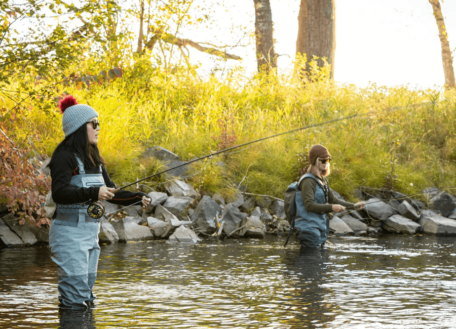 two women standing in a river fly fishing with warm alpaca wool clothing