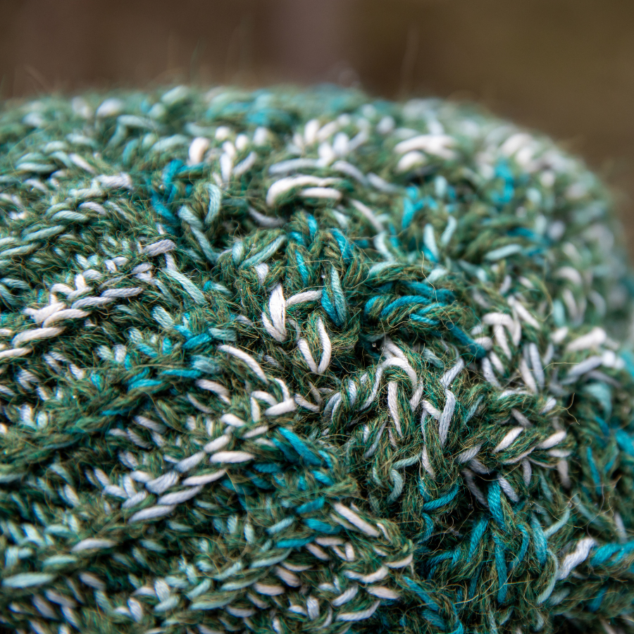 A close up photograph of the warm cozy handmade knit crochet Alpacas of Montana celtic hat, a mixture of the colors moss green, teal, turquoise, seafoam, and white.