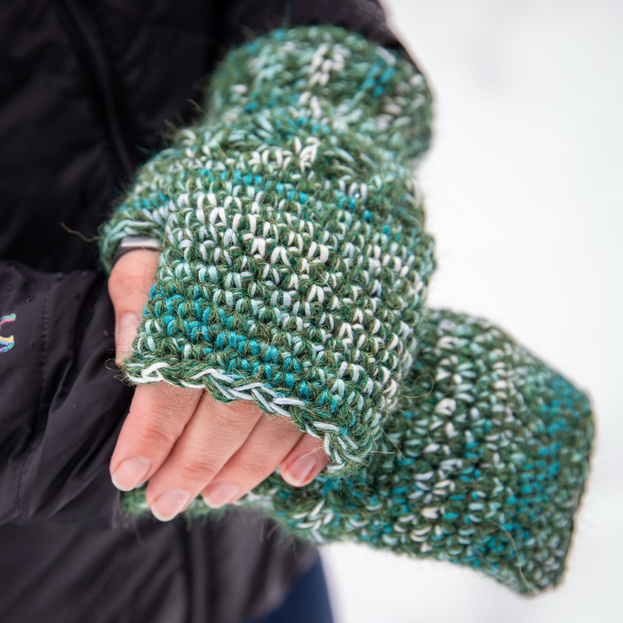 A close up photograph of the warm cozy handmade alpaca yarn and bamboo yarn knitted crochet Alpacas of Montana fingerless celtic wristie mittens, a mixture of the colors moss green, teal, turquoise, seafoam, and white.