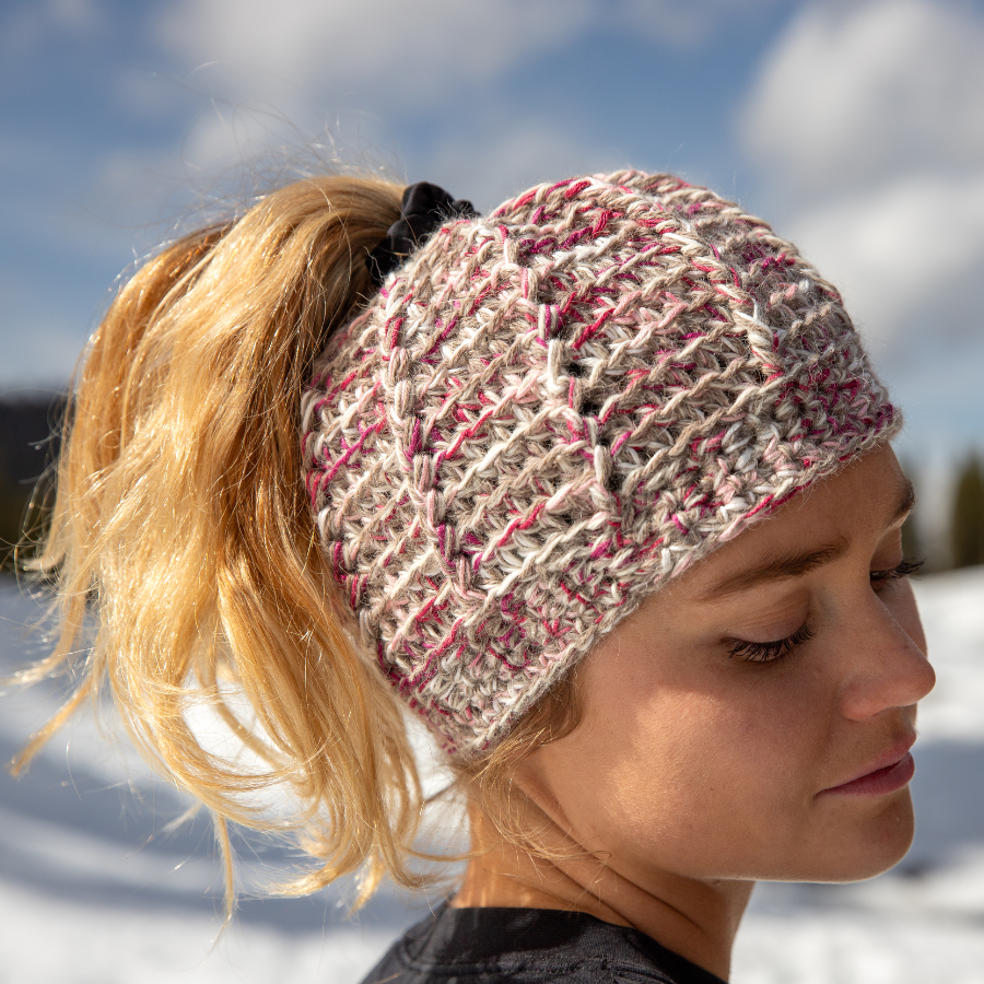 A close up of a blonde woman wearing a A product photo on a white background of a soft cozy comfortable fashionable moisture wicking knitted crochet ponytail hat handmade in Montana from natural white, latte brown, and light pink blush alpaca wool and bamboo yarn.