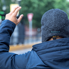 A person facing away from the camera wearing a navy jacket and a dark gray extremely warm cozy soft windproof comfortable moisture wicking thermal winter alpaca fleece wool city commuter hat.