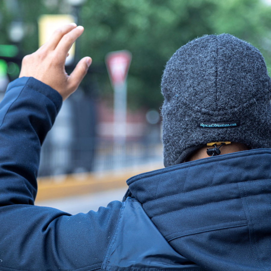A person facing away from the camera wearing a navy jacket and a dark gray extremely warm cozy soft windproof comfortable moisture wicking thermal winter alpaca fleece wool city commuter hat.
