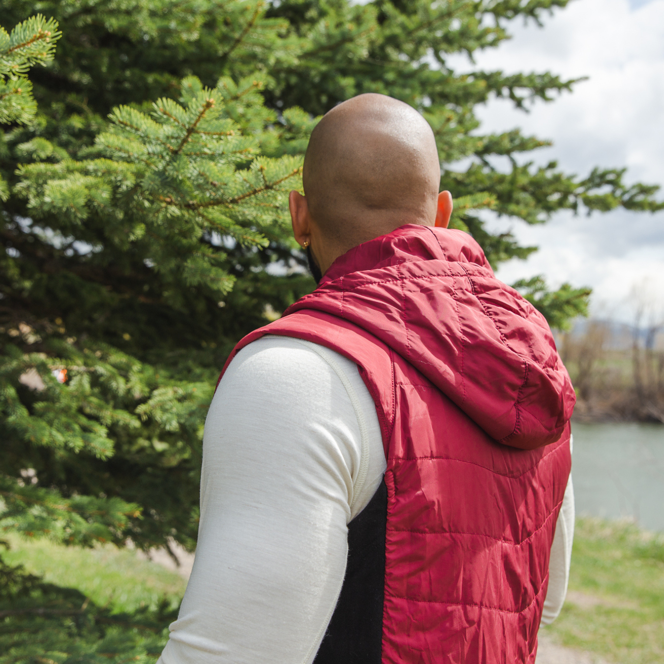 A photo of a bald man facing away from the camera wearing an Alpacas of Montana natural white men's long sleeve performance tee and a cranberry red Alpacas of Montana lightweight athletic activewear outerwear breathable moisture wicking antimicrobial soft comfortable exercise alpaca men's stretch lite vest for running sports exercise work out hiking climbing camping biking