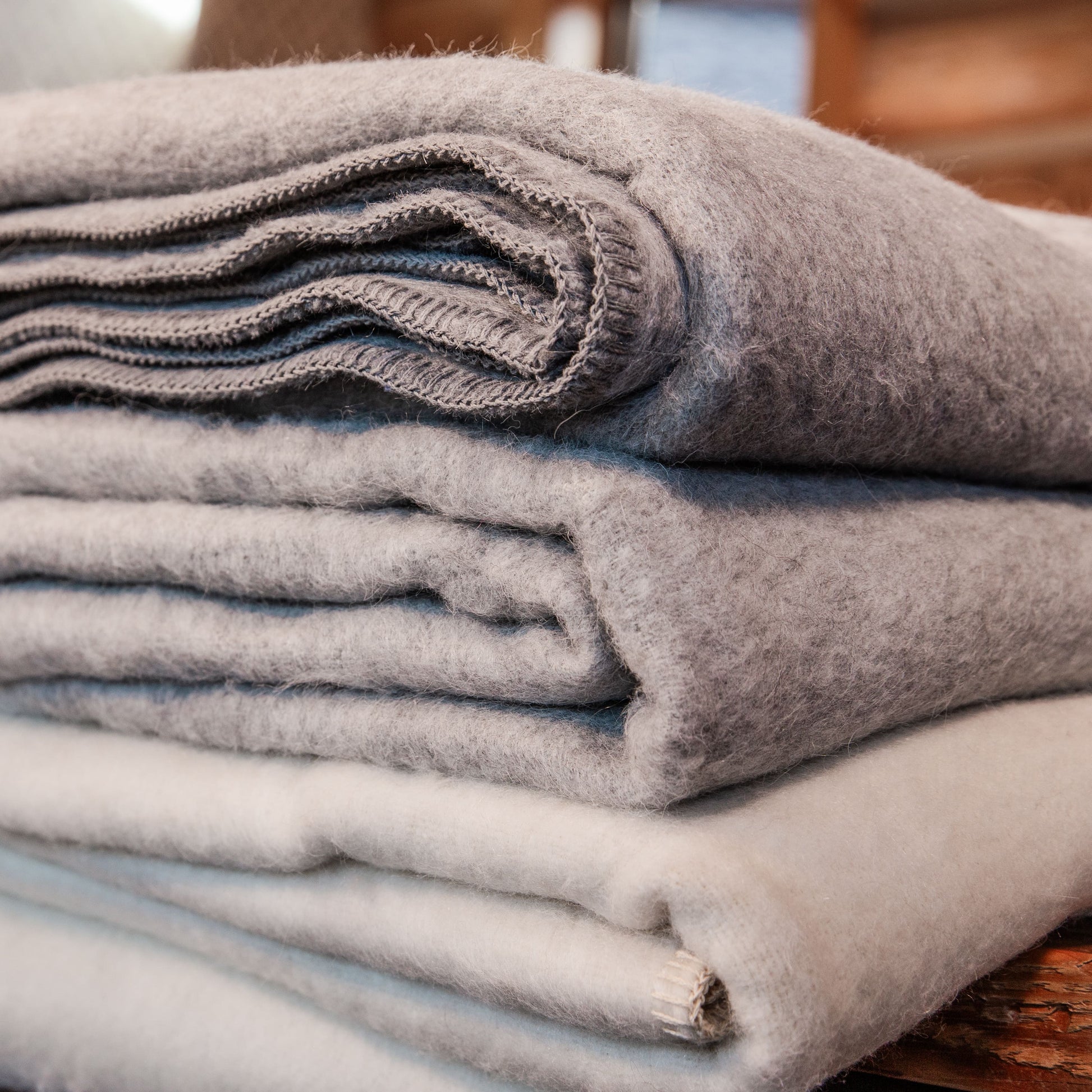 A close up photo of a stack of medium gray, light gray, and natural white soft cozy moisture wicking warm Alpacas of Montana alpaca wool king and queen size blankets.