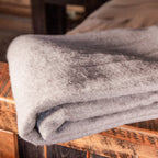A close up shot of a folded light gray Alpacas of Montana soft warm thermal moisture wicking lightweight plush king or queen size alpaca wool blanket.