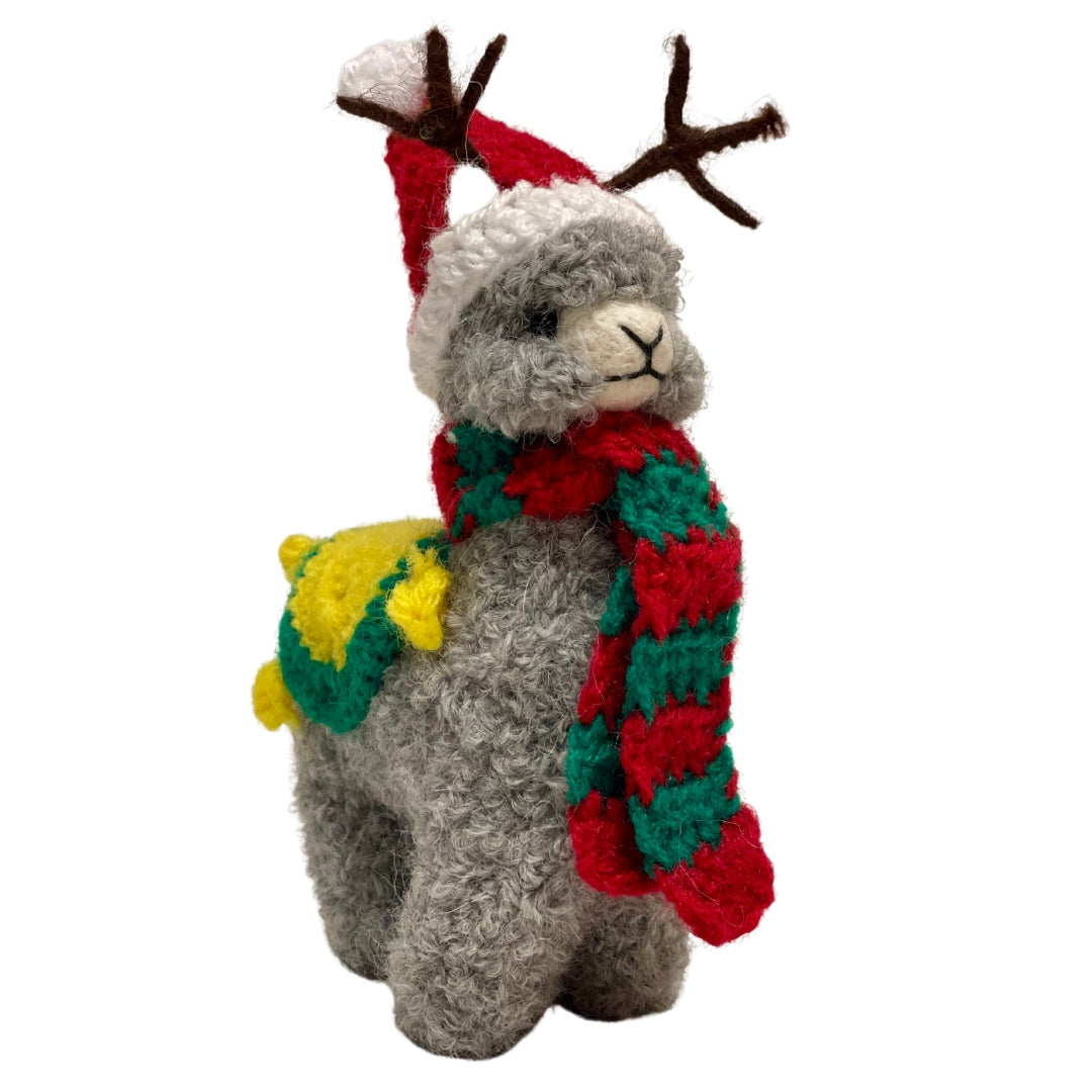 A product photo of a cute soft fluffy handmade toy light gray alpaca with brown antlers, a red and white santa hat, a red and green scarf, and a yellow and green blanket felted woven alpaca wool figurine and ornament for christmas holiday gifts
