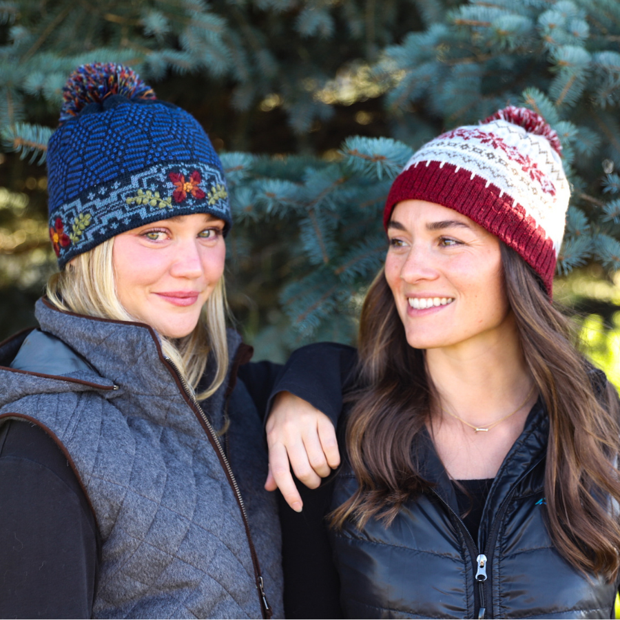 Two women wearing colorful knit hats outdoors with trees in the background