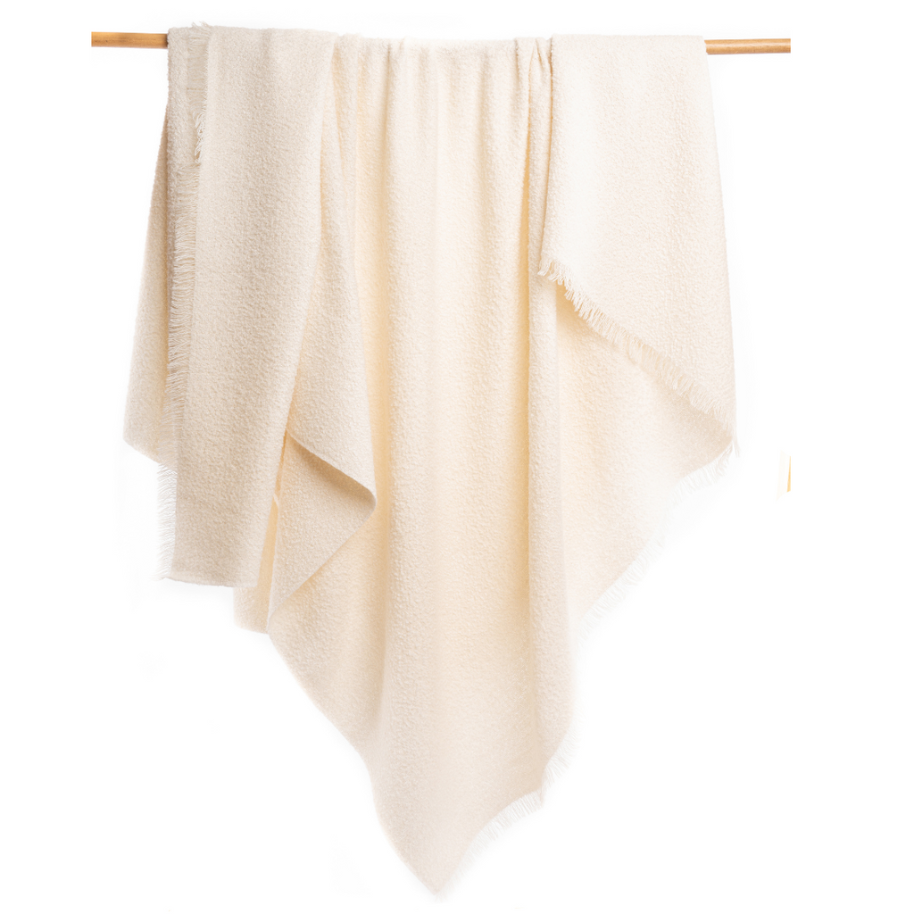 An Alpacas of Montana soft cozy luxury warm natural white boucle plush blanket with a tasseled edge.