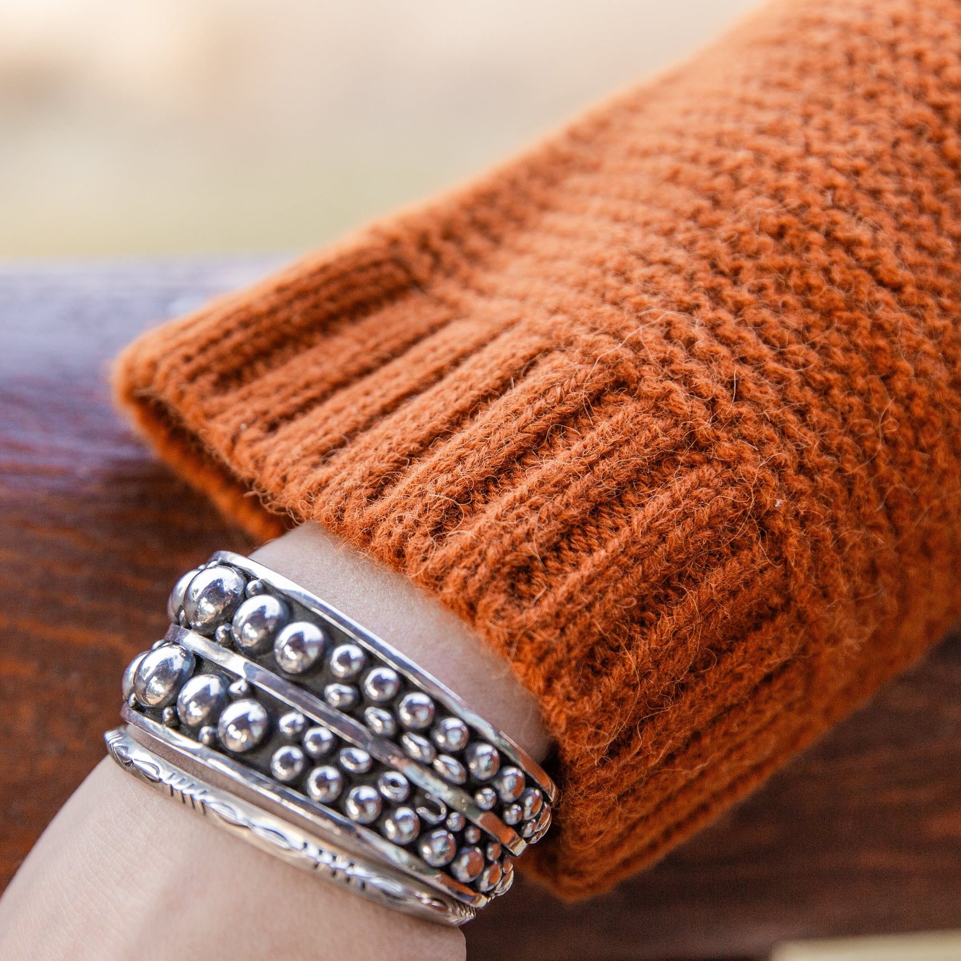 A close-up of a woman's wrist wearing silver bracelets and the soft comfortable cute fashionable cozy sweater in the color autumn orange.