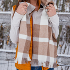 A shoulders-down photo of a person in front of a wooden fence wearing an orange puffy vest over a long sleeve white shirt and and a beautiful soft cozy luxury stylish fashion comfortable accessory chestnut brown, light gray, and natural white alpaca wool scarf with tassels.