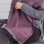 A close up photo of a person wearing black pants, a gray long sleeved shirt, and a soft cozy stylish comfortable women's fashion moisture wicking warm cute lovely herringbone patterned plum purple violet and gray alpaca wool scarf.