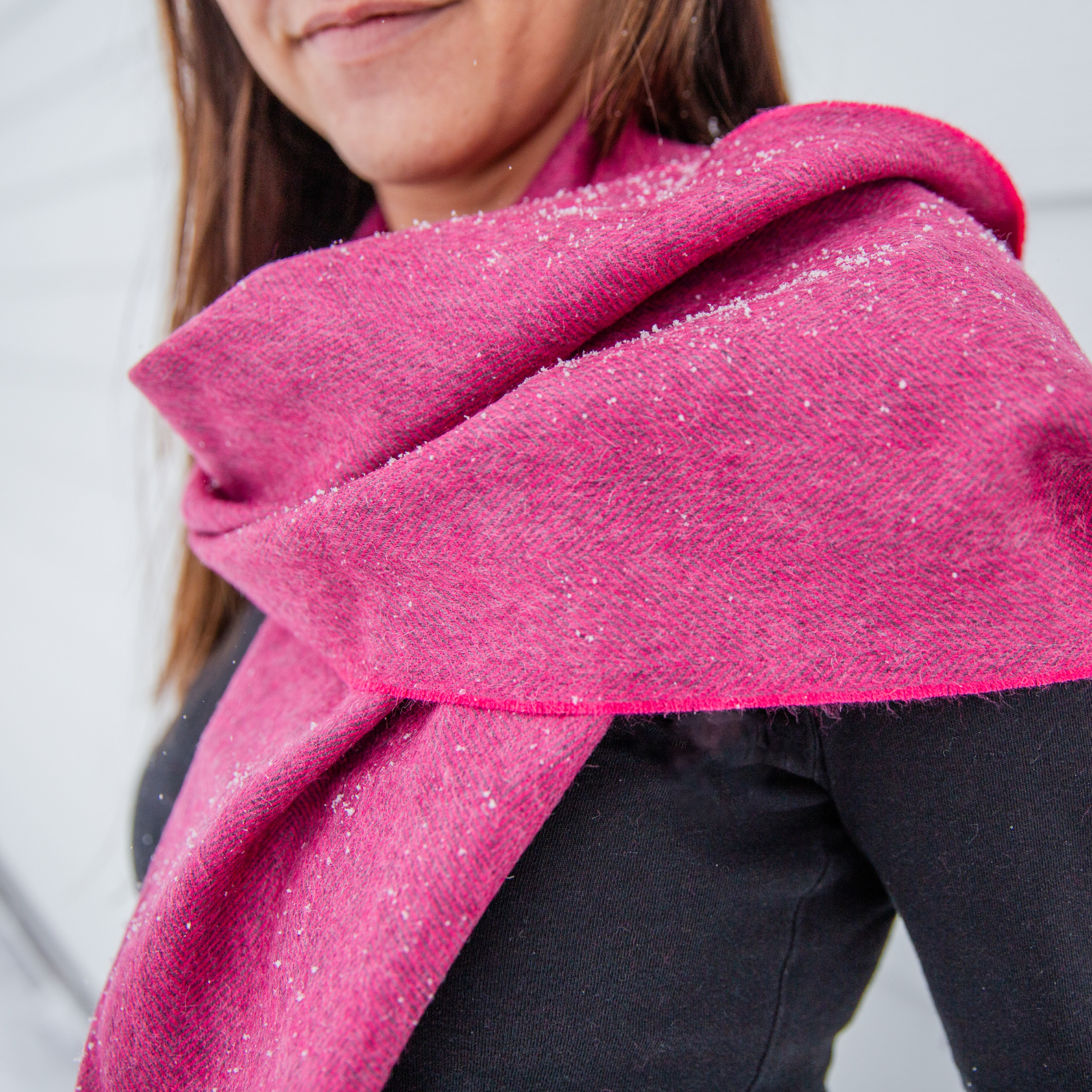 A close up photo of a brown haired woman wearing a black long sleeve shirt and a soft cozy stylish comfortable women's fashion moisture wicking warm cute lovely herringbone patterned fuchsia pink and gray alpaca wool scarf.