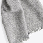 A close up product photo with a white background of a soft cozy stylish comfortable women's fashion moisture wicking warm cute lovely herringbone patterned gray alpaca wool scarf.