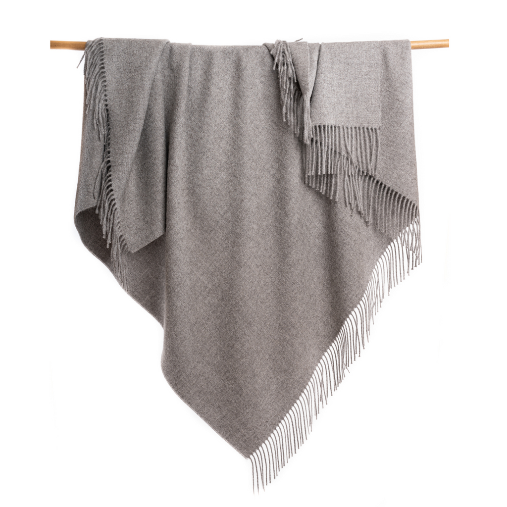 An Alpacas of Montana soft cozy luxury warm medium light charcoal gray blanket with a tasseled edge.