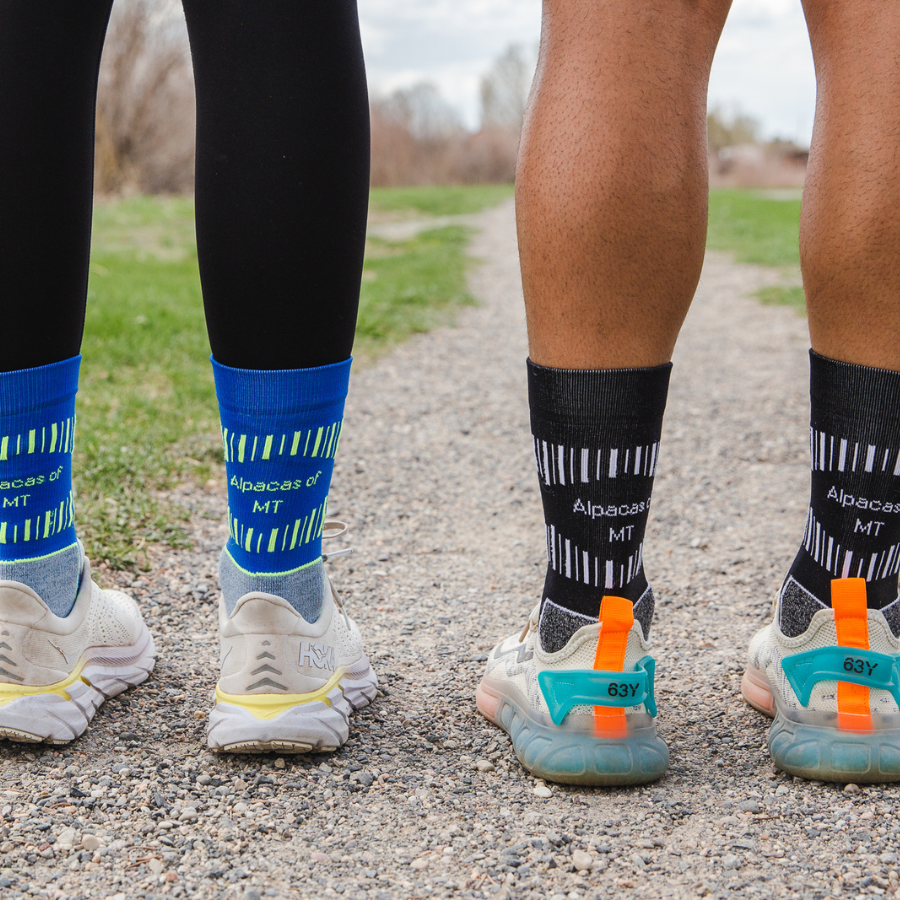A close up photo of two people's feet wearing running shoes and Alpacas of Montana soft cozy comfortable activewear outerwear athletic workout moisture wicking antimicrobial cushioned light compression engineered high-tech mid-crew hiking sock for walking, skiing, climbing, hunting, camping, fishing, exercise, biking