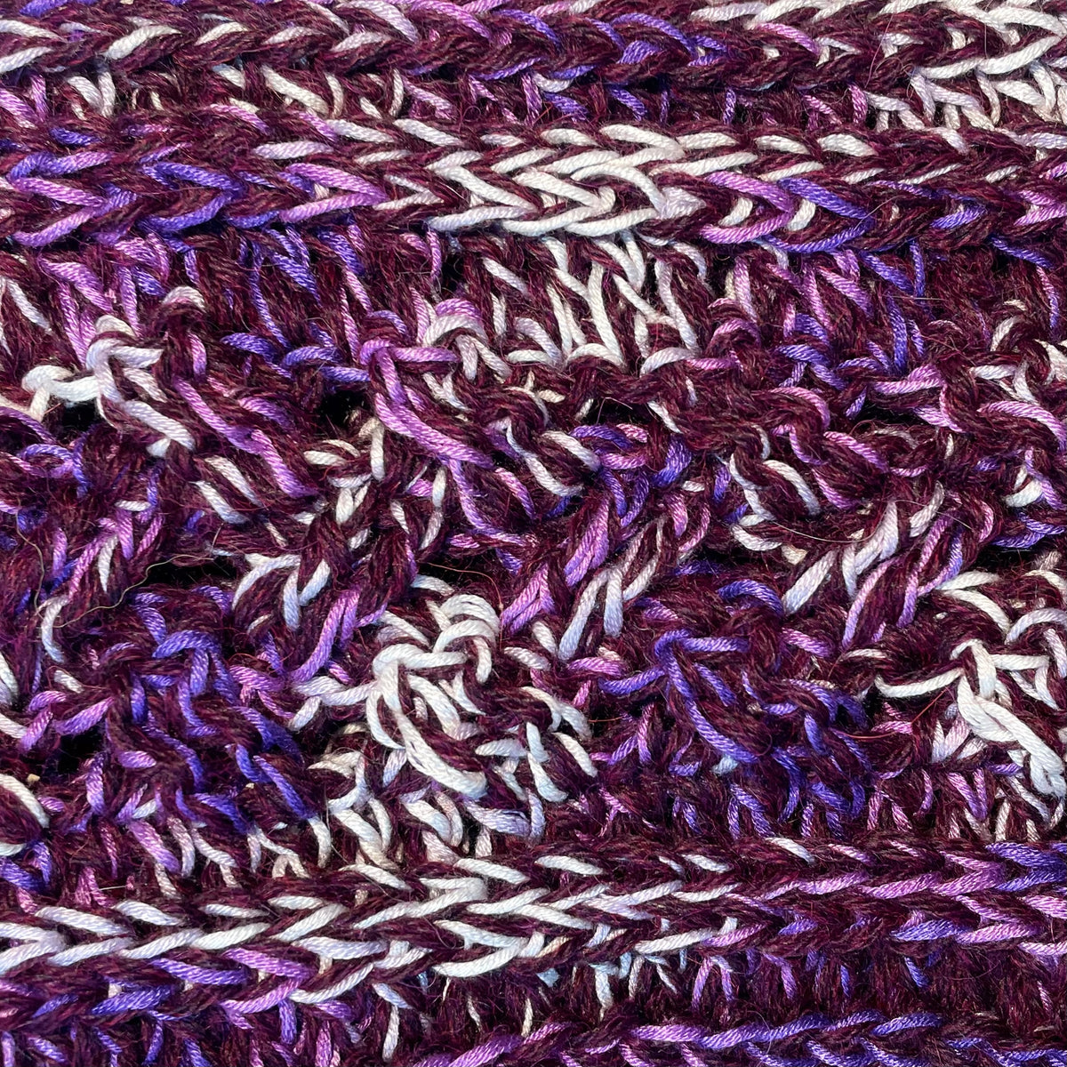 A close up photograph of the warm cozy handmade knit crochet Alpacas of Montana scarf, a mixture of deep purple, bright violet, and white.