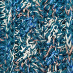 A close up photograph of the warm cozy handmade knit crochet Alpacas of Montana scarf, a mixture of the colors ocean blue, dark turquoise, cobalt, cerulean, gray, and white. 