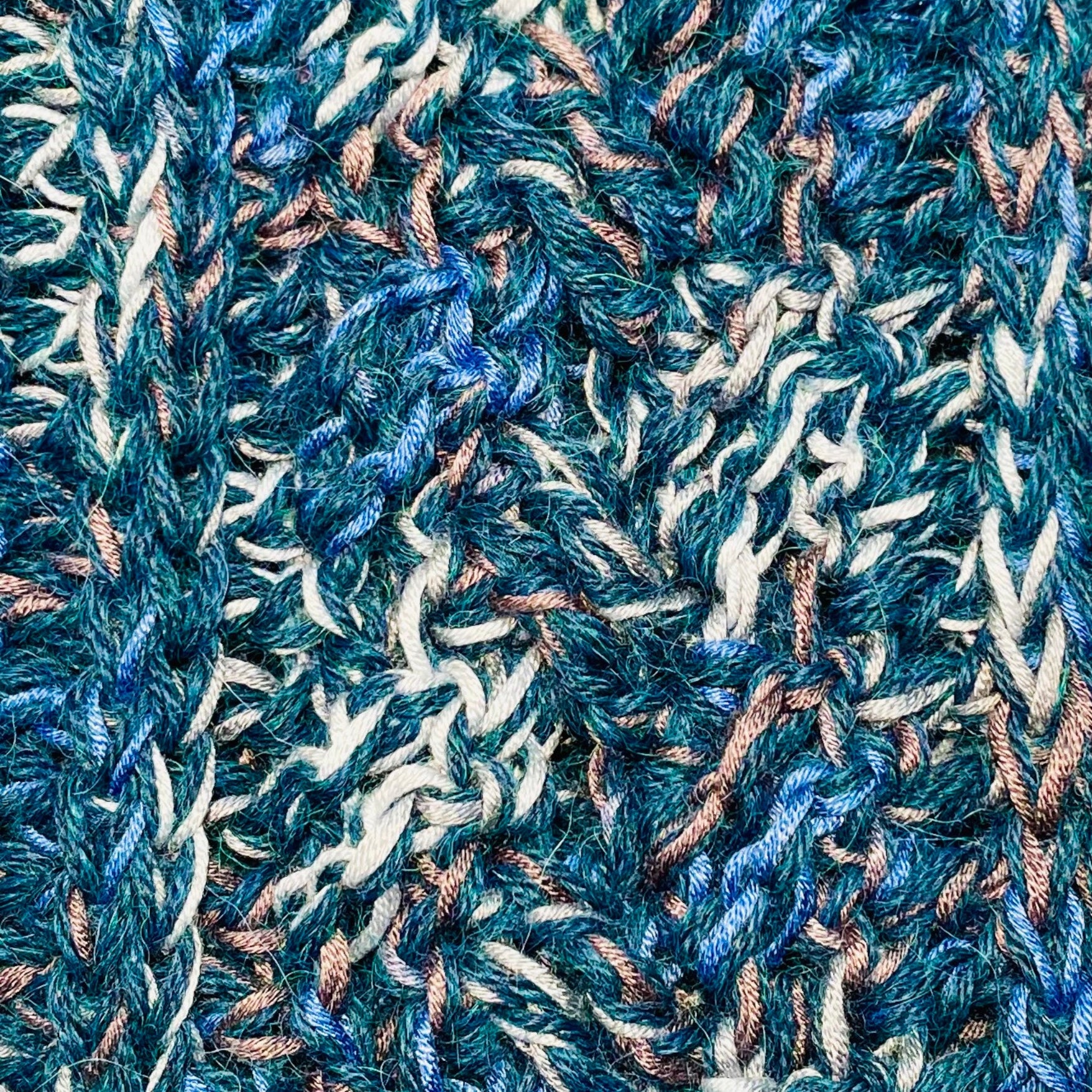 A close up photograph of the warm cozy handmade knit crochet Alpacas of Montana scarf, a mixture of the colors ocean blue, dark turquoise, cobalt, cerulean, gray, and white. 
