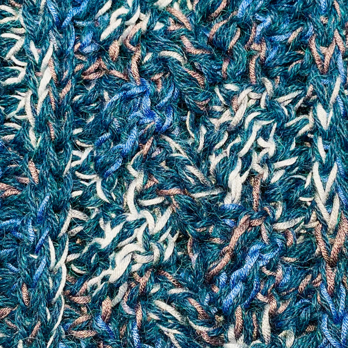A close up photograph of the warm cozy handmade knit crochet Alpacas of Montana scarf, a mixture of the colors ocean blue, dark turquoise, cobalt, cerulean, gray, and white. 