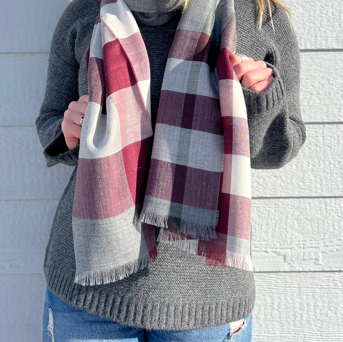 A torso-only photo of a woman wearing a charcoal gray Alpacas of Montana Cozy Knit Sweater and a soft comfortable cozy lightweight elegant fashion beautiful silk and alpaca wool woven maroon, light gray, and white scarf.