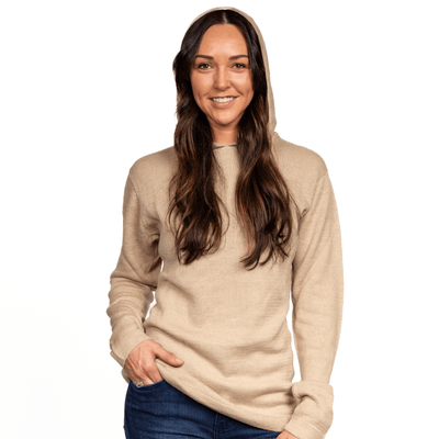 A woman wearing a beige alpaca hoodie, smiling and posing for the camera.