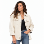 A woman modeling a cream-colored textured jacket over a black top and blue jeans, photographed against a solid white background.