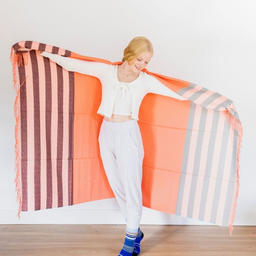 woman smiling with arms extended holding tangerine alpaca wool blanket with stripes