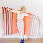 woman smiling with arms extended holding tangerine alpaca wool blanket with stripes