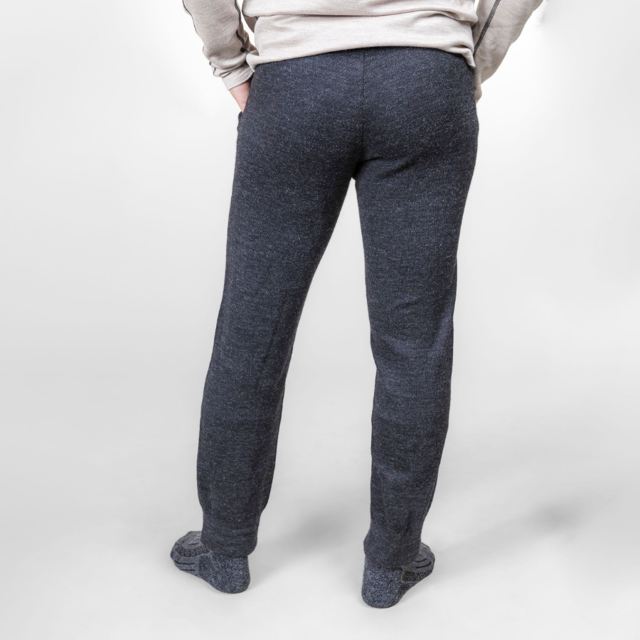 A waist-down photo of a man standing against a white background. He is wearing gray Alpacas of Montana adventure hiking socks and charcoal gray Alpacas of Montana soft cozy comfortable lightweight lounge moisture wicking antimicrobial exercise men's joggers sweatpants made from alpaca wool for lounging, comfort, exercise, hiking, skiing