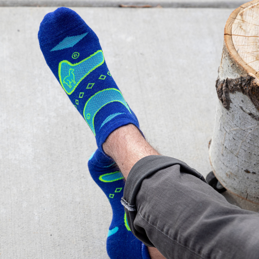 A close up photo of a pair of feet wearing a pair of Alpacas of Montana soft comfortable breathable athletic outerwear activewear moisture wicking blue, cyan, and lime yellow endurance sock for running, sports, hiking, exercise.
