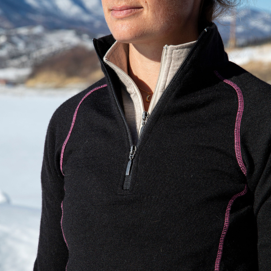 A close up photo of the zipper of a black with pink stitching Alpacas of Montana warm thermal soft cozy comfortable activewear outerwear athletic moisture wicking antimicrobial women's fashion stylish luxury mid-layer quarter-zip alpaca wool long sleeve pullover top for outdoors camping climbing hiking skiing hunting fishing running winter.