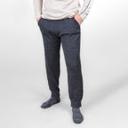 A man standing in front of a white background wearing an oatmeal Alpacas of Montana men's base layer top, gray Alpacas of Montana adventure hiking socks, and charcoal gray Alpacas of Montana soft cozy comfortable lightweight lounge moisture wicking antimicrobial exercise men's joggers sweatpants made from alpaca wool for lounging, comfort, exercise, hiking, skiing