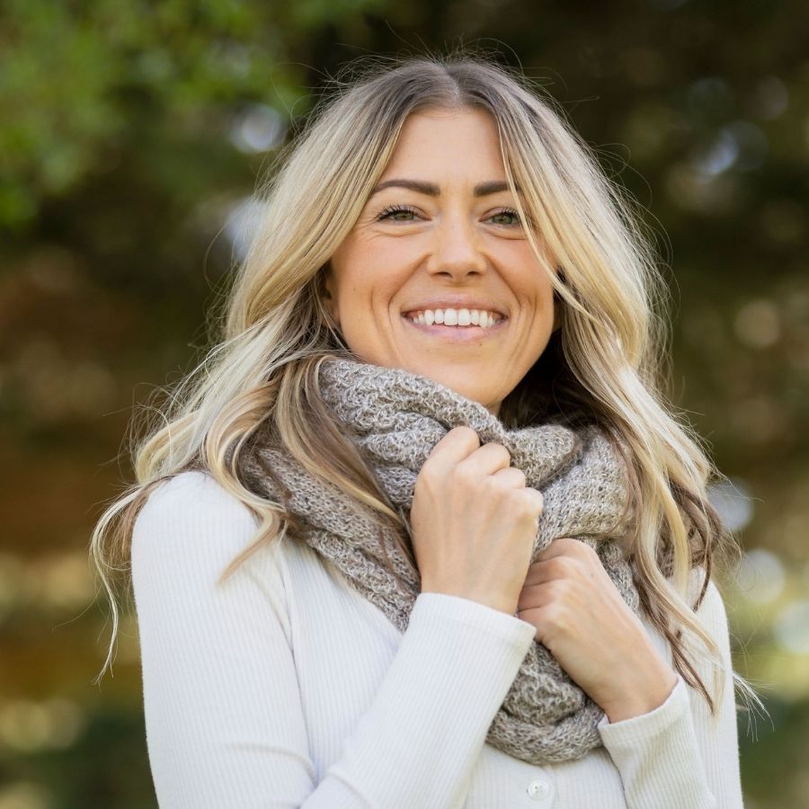 woman smiling and standing outside wearing oatmeal alpaca wool infinity scarf