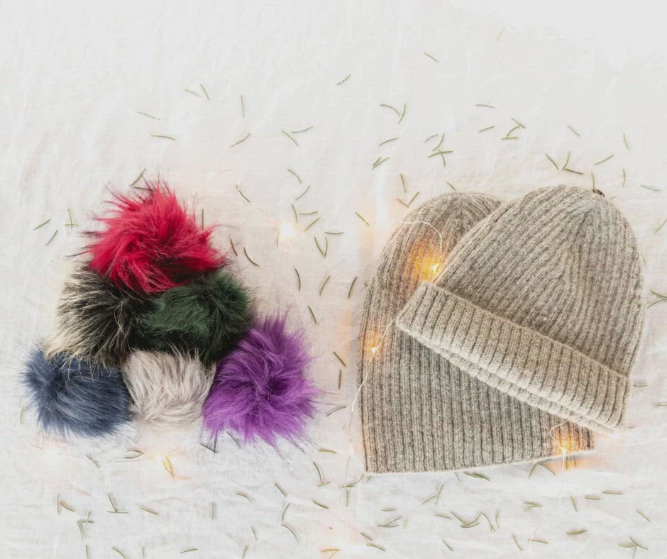 A stop motion gif of a red and a green pom pom moving over to sit on the top of ribbed Beartooth Beanies