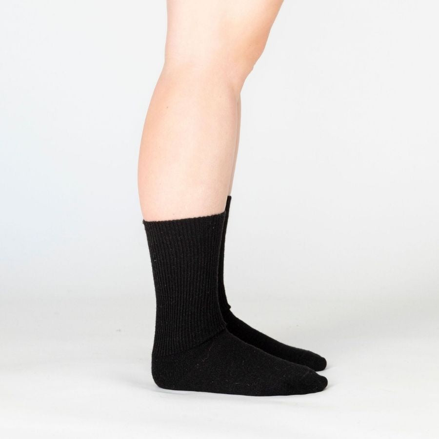 Side view of a person&#39;s lower legs against a white background wearing black Alpacas of Montana professional soft comfortable moisture wicking business casual alpaca wool dress socks for men and women.