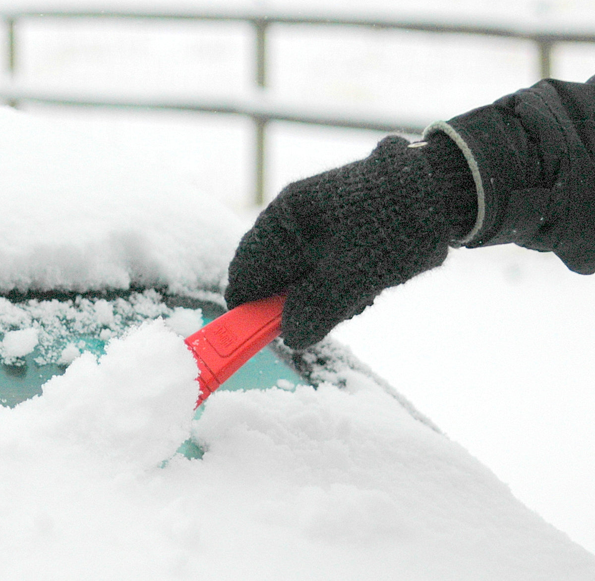 man scraping snow off of car windshield with gray mittens for winter