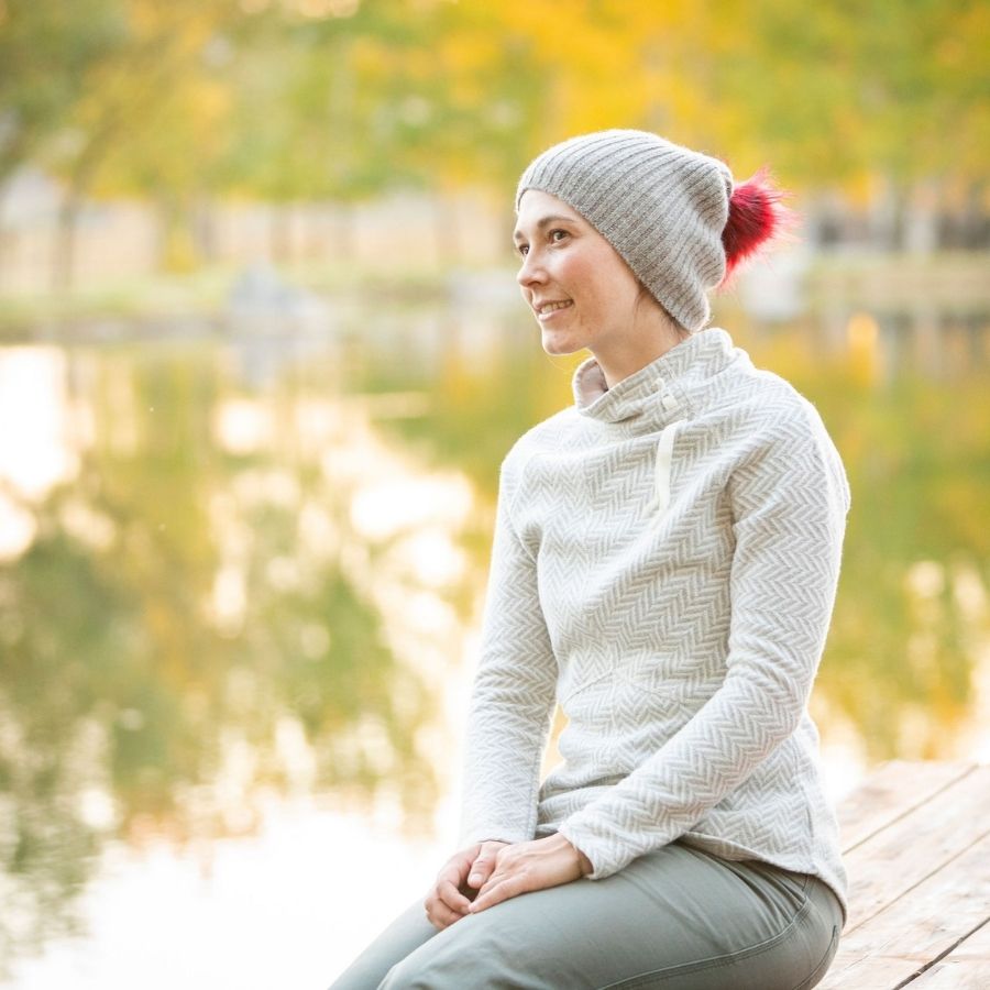 woman sitting on a dock in the fall wearing gray ribbed alpaca wool beartooth beanie with red pom pom