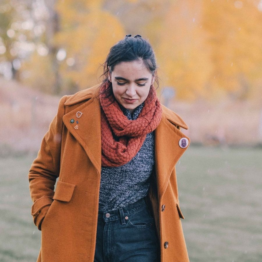woman walking outside in the fall looking down and wearing alpaca wool rusty orange infinity scarf