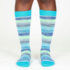 A person's lower legs with a white background wearing Alpacas of Montana colorful navy, cobalt, sky blue, lime green, gray, and black casual lounge fashion comfortable soft cozy everyday moisture wicking alpaca wool striped socks.