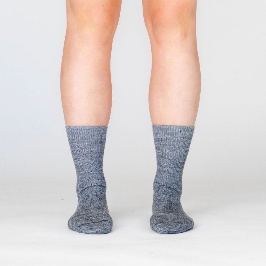 person&#39;s lower legs wearing medium gray alpaca wool dress socks against white background