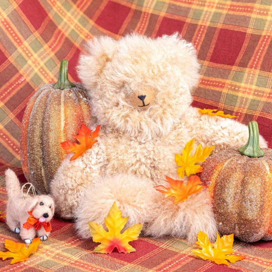 A red and orange plaid cloth with decorative pumpkins, autumn leaves, and an Alpacas of Montana soft fluffy cozy cute adorable toy silky tan beige fawn luxury royal alpaca teddy bear plushie figurine for gifts birthdays christmas children alll ages.