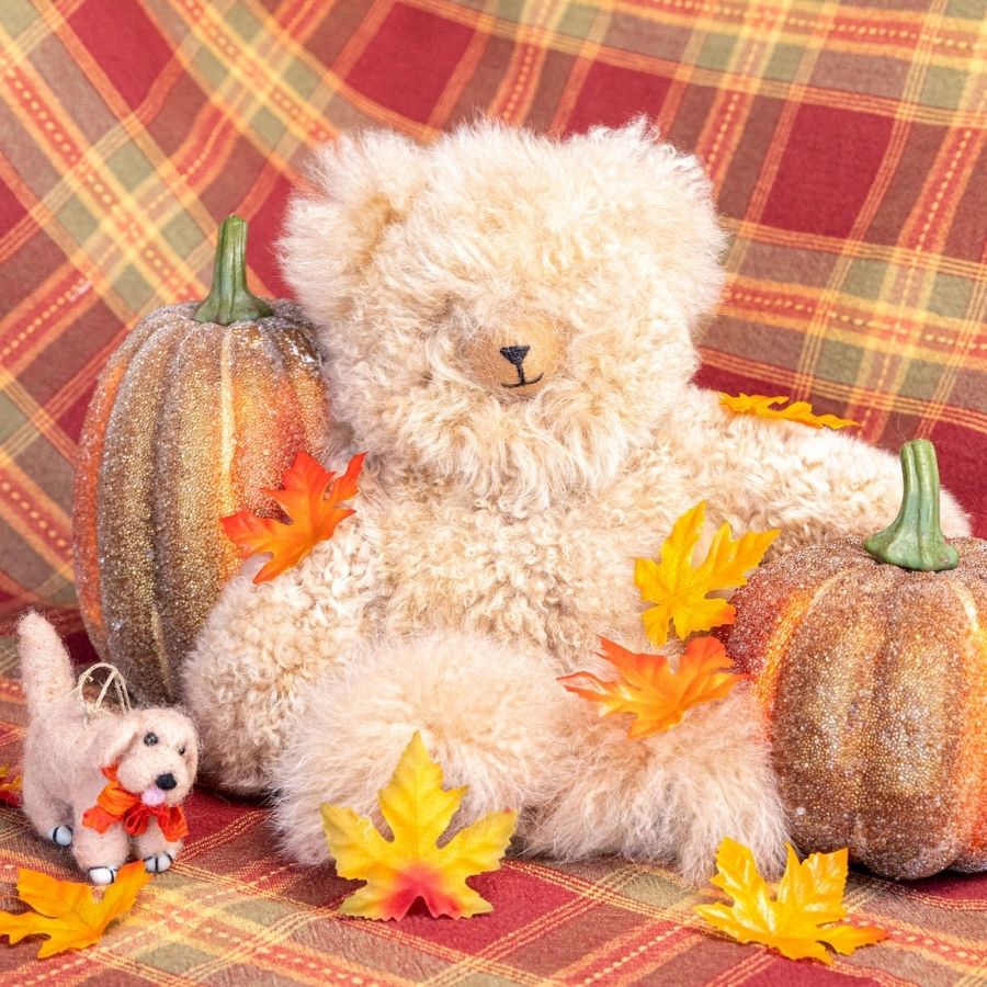 beige alpaca wool teddy bear sitting with pumpkins and yellow leaves