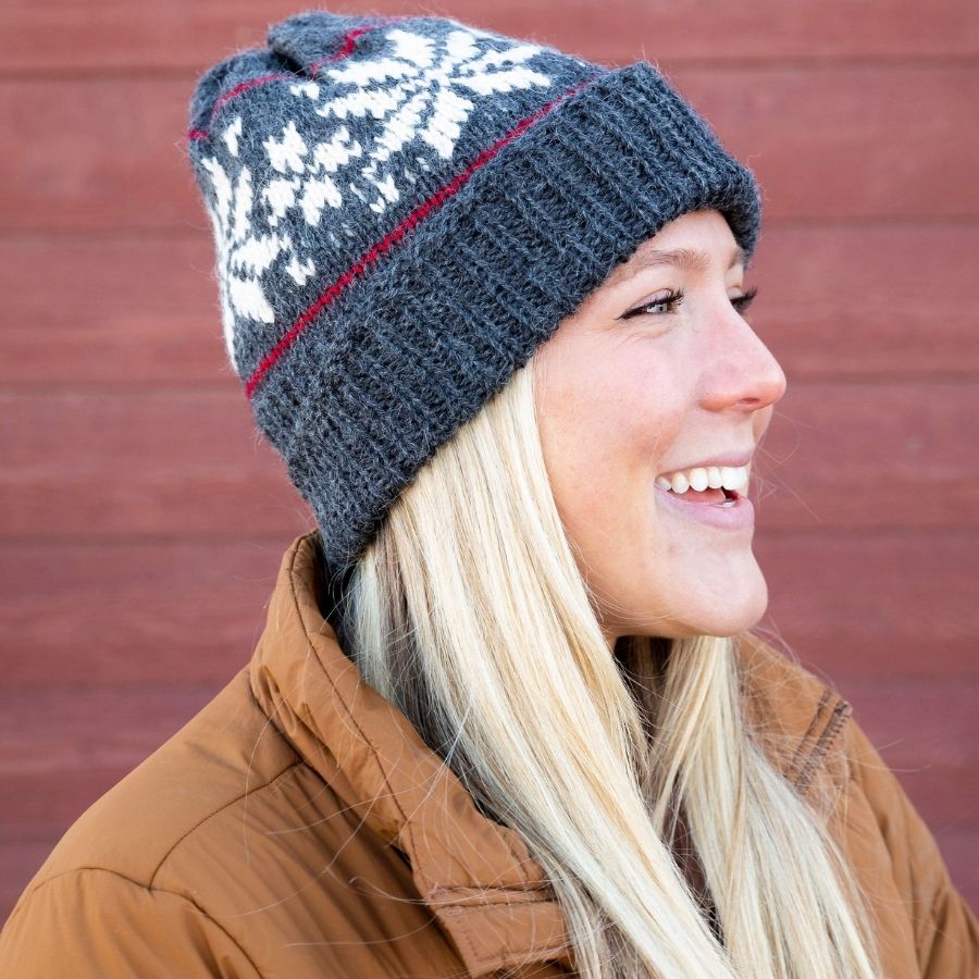 woman smiling wearing gray alpaca wool beanie hat with white snowflakes and red stripes