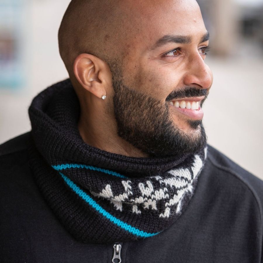 man looking to his side wearing handmade black alpaca wool cowl with teal stripes and white snowflakes