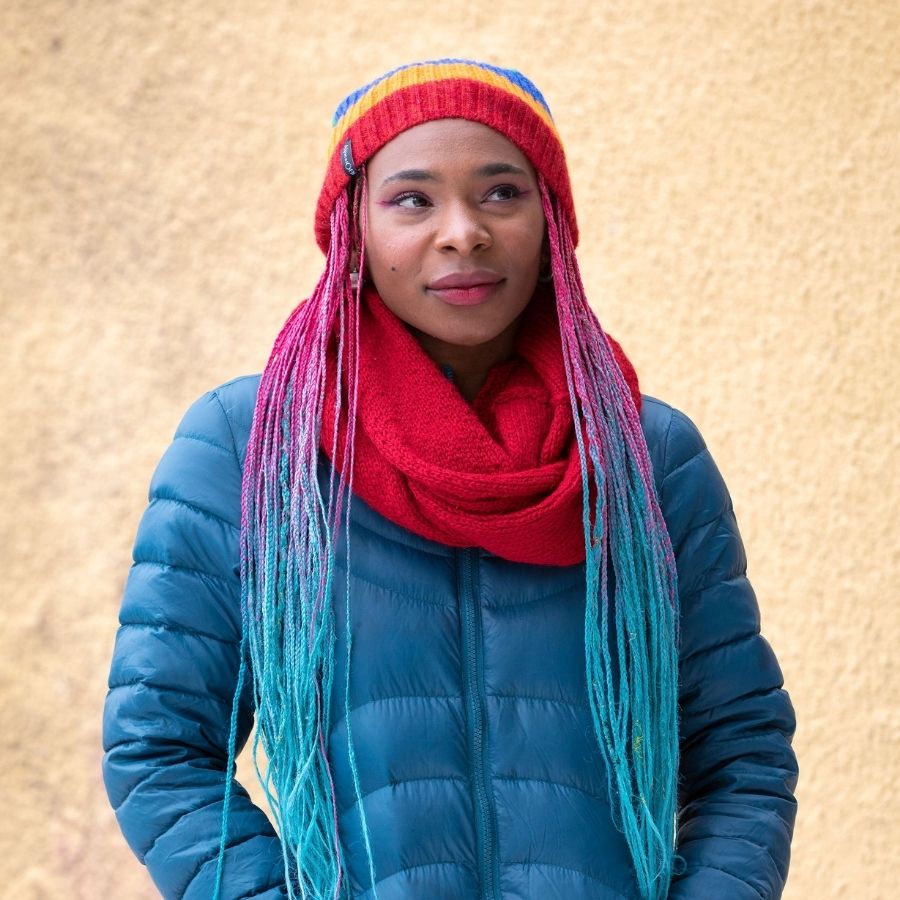 woman standing with her hands in her pockets wearing handmade red alpaca wool infinity scarf and blue puffy coat