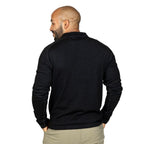 A smiling bald man with a black beard standing facing away from the camera with his hands in his pockets in front of a white background. He is wearing khaki pants and a black Alpacas of Montana warm thermal soft cozy comfortable activewear outerwear athletic moisture wicking antimicrobial men's fashion stylish luxury mid-layer quarter-zip alpaca wool long sleeve pullover top for outdoors camping climbing hiking skiing hunting fishing running winter.