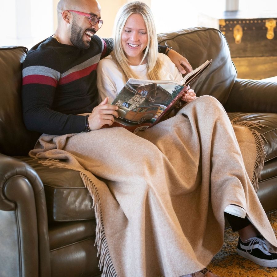 man and woman sitting on the couch reading a book while wrapped in warm honey alpaca wool blanket