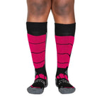 A person's lower legs with a white background wearing fuchsia pink, gray, and black Alpacas of Montana cozy comfortable soft warm thermal winter freezing temperatures antimicrobial moisture wicking alpaca wool ski and snowboard socks for snowshoeing, skiing, snowboarding, ice fishing, outdoors.